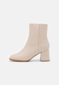 Beige semišové kotníkové boty s blokovým podpatkem a čtveratým špičkou, zobrazené v profilu na bílém pozadí.