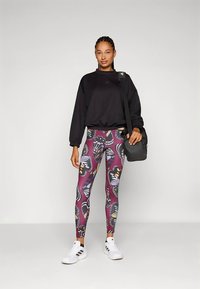 Zwart sweatshirt met lange mouwen, gecombineerd met kleurrijke, patroonleggings met vlinders. Ze draagt een kleine zwarte tas en witte sneakers.