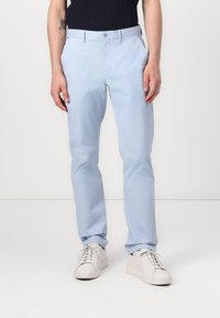 Chinos en coton bleu clair avec une coupe slim, dotés de poches latérales, de passants de ceinture et d'une texture lisse. Associés à des baskets blanches.