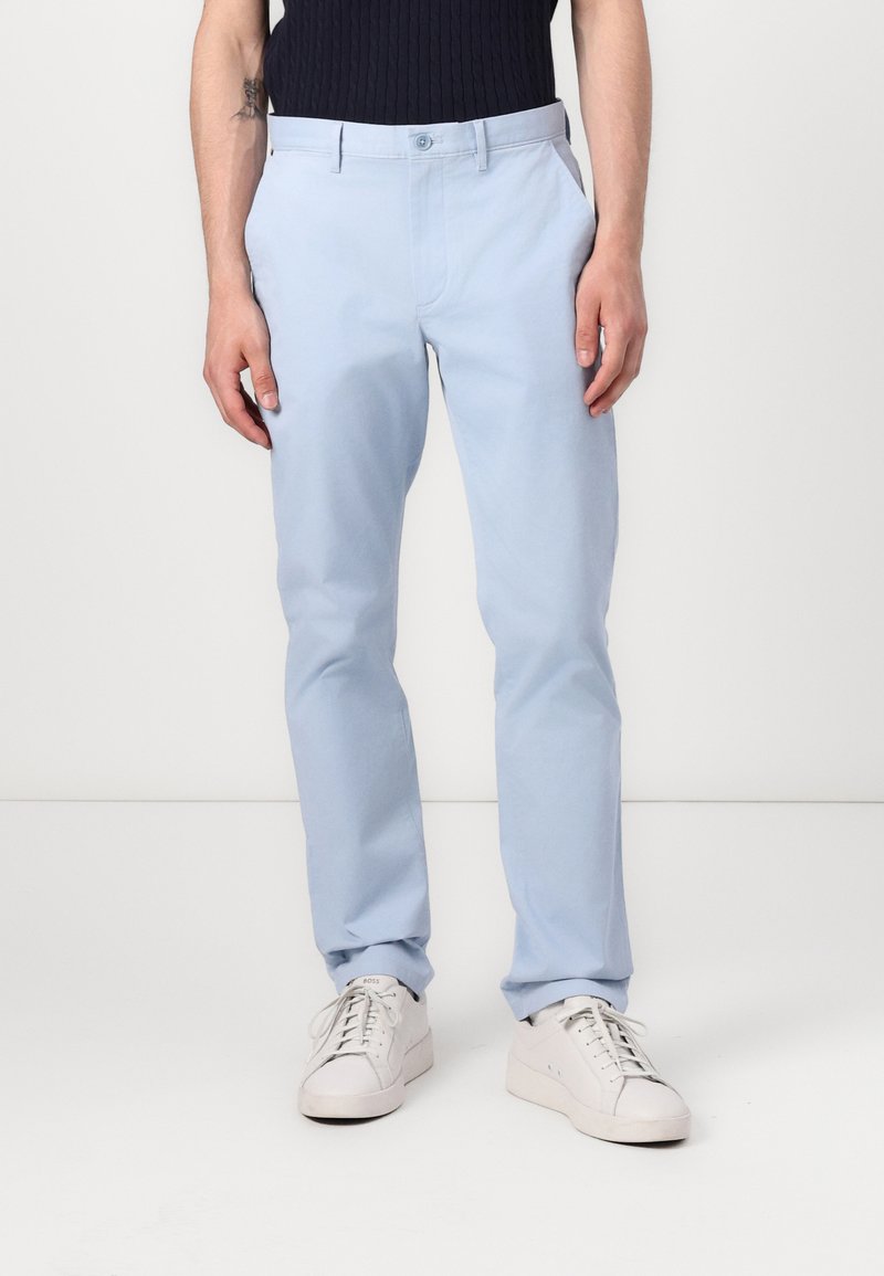 Chinos en coton bleu clair avec une coupe slim, dotés de poches latérales, de passants de ceinture et d'une texture lisse. Associés à des baskets blanches.