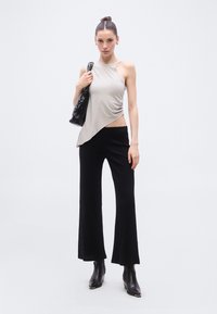 Αμάνικο ασύμμετρο μπεζ τοπ σε συνδυασμό με μαύρο παντελόνι φαρδιάς γραμμής με ριμπ ύφανση. Το μοντέλο κρατά μια λαμπερή μαύρη τσάντα. Ομαλές υφές και καθαρές γραμμές.