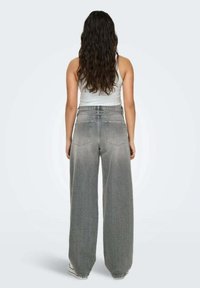 Jeans in denim grigio a gamba larga con una finitura leggermente sbiadita, design a vita alta e due tasche posteriori, indossati con un top aderente bianco.