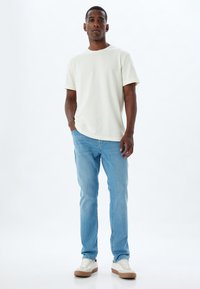 Camiseta de algodón color beige claro, de corte relajado, combinada con jeans de mezclilla azul claro. Zapatillas blancas con suelas de color beige. Diseño simple y limpio.