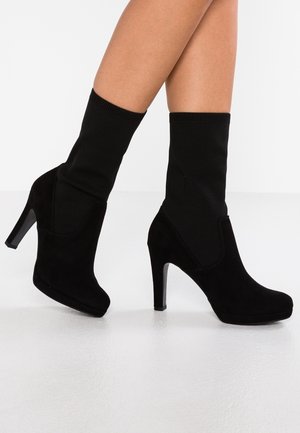 Zwarte enkellaarzen met een suede textuur en hoge stilettohak. Heeft een gebreide zwarte sokachtige bovenkant voor een snug fit en moderne stijl.