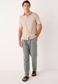 Kortærmet button-up skjorte med blomstermønster i beige og orange, parret med grå bukser og brune sandaler. Minimalistisk design.