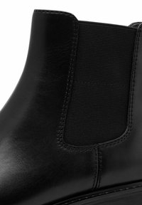 Bottine en cuir noir avec panneau latéral élastique, texture lisse, coutures renforcées et bout arrondi. Design minimaliste, look classique.