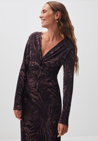 Langärmliges Kleid aus dunkelviolettem Stoff mit gerippter Textur. Verfügt über einen V-Ausschnitt und ein gewickeltes Knotendetail an der Taille, gemustert in Beige-Tönen.