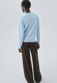 Un pull bleu clair avec des manches longues et une coupe décontractée, associé à un pantalon marron à jambes larges. La texture semble douce et lisse.