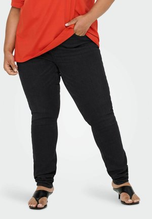 Czarne skinny jeans wykonane z denimu, z średnim stanem i gładką fakturą. Połączone z luźną czerwoną bluzką i czarnymi sandałami z odkrytymi palcami.