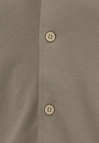 Camicia button-up beige realizzata in tessuto testurizzato, con quattro bottoni arrotondati lungo la patta e una finitura liscia.