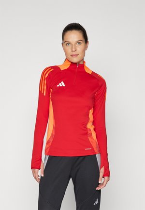 Rotes langärmliges Sportoberteil mit orangefarbenen Akzenten, Viertelreißverschluss, drei weißen Streifen auf der Schulter und einem Etikett für atmungsaktives Material.