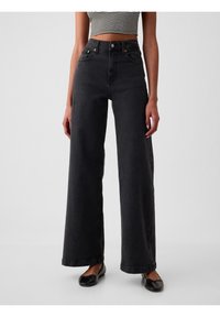 Jean noir taille haute à jambes larges en denim. Comprend des poches avant, des accents en métal et un ourlet net.