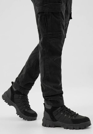 Černé termoskové boty na turistiku vyrobené z kombinace texturovaných materiálů. Mají robustní podešve, šněrování a polstrovaný kotník pro podporu.