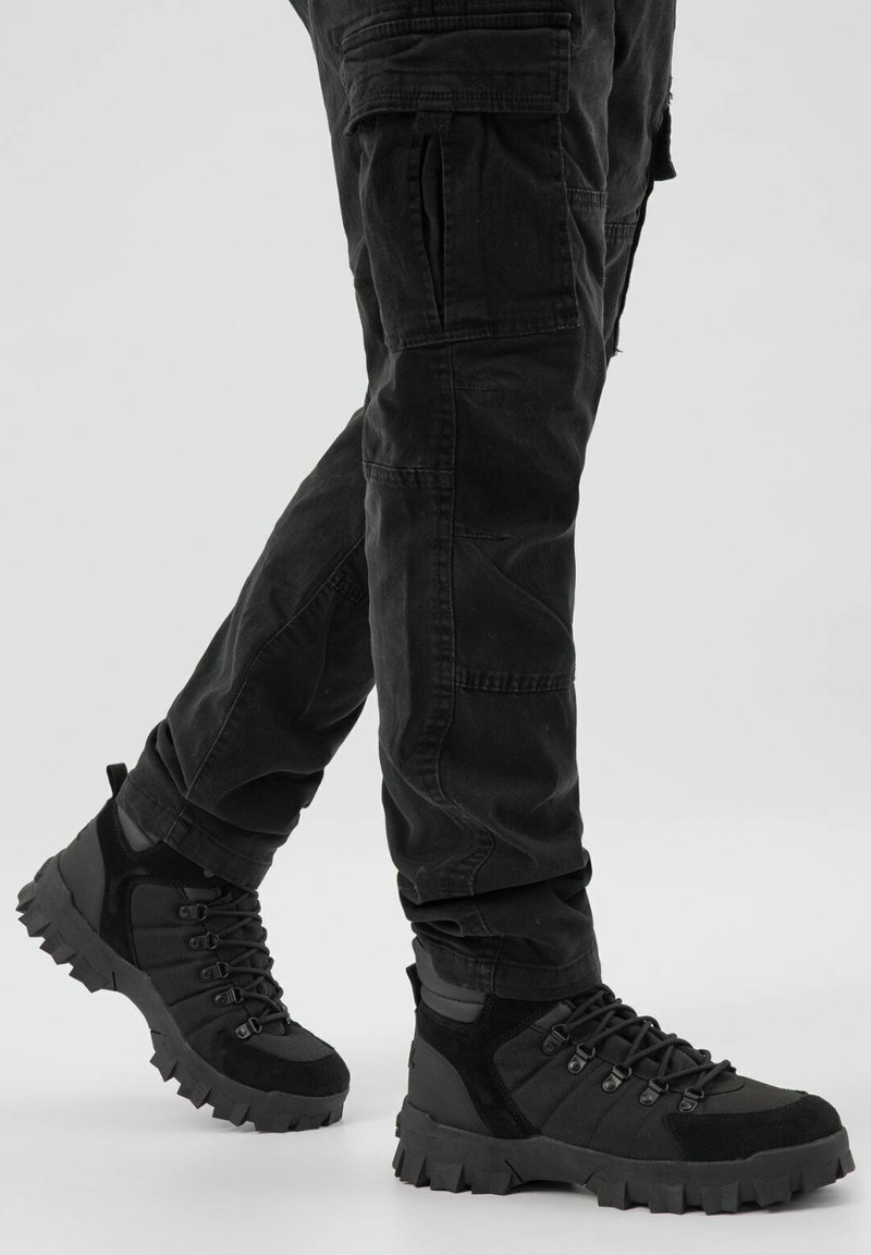 Černé termoskové boty na turistiku vyrobené z kombinace texturovaných materiálů. Mají robustní podešve, šněrování a polstrovaný kotník pro podporu.