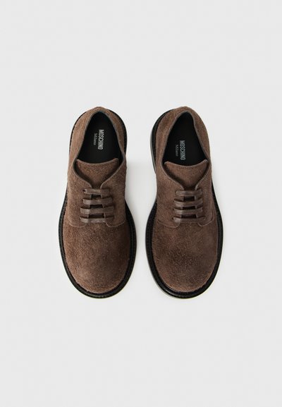 Zapatos de ante marrón con cordones, con puntera redonda, parte superior texturizada y suela de cuero negro liso. Presenta seis ojetes para los cordones.