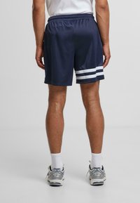 Shorts de sport bleu marine en tissu léger. Présentent des accents rayés blancs sur les côtés et une taille élastique pour le confort.
