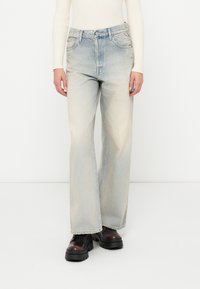 Šviesiai mėlyni platūs džinsai iš džinsinio audinio su išblukusiomis vietomis ir klasikiniu penkių kišenių dizainu. Yra diržo kilpos ir zip užtrauktukas.