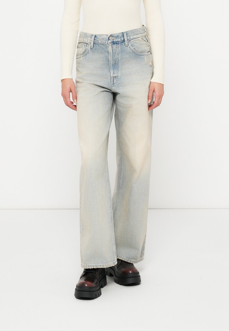 Šviesiai mėlyni platūs džinsai iš džinsinio audinio su išblukusiomis vietomis ir klasikiniu penkių kišenių dizainu. Yra diržo kilpos ir zip užtrauktukas.