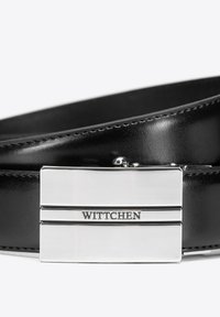 Schwarzer Ledergürtel mit einer rechteckigen silbernen Metallschnalle, die die eingravierte Aufschrift "WITTCHEN" und zwei horizontale Linien auf der Vorderseite zeigt.