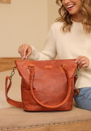 Brown leather tote bag with two rounded handles and a detachable shoulder strap. Features a zippered top and subtle textured finish.