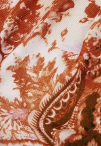 Tessuto con motivo floreale in tonalità rosso-bruno su sfondo crema, con una superficie testurizzata e finitura morbida.