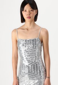 Silver sequin dress with thin shoulder straps, featuring a geometric pattern and a fitted silhouette. Smooth texture with shiny accents.