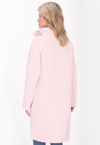 Cappotto in pile rosa chiaro con colletto alto, maniche lunghe e vestibilità ampia, caratterizzato da una texture sottile e tasche laterali.