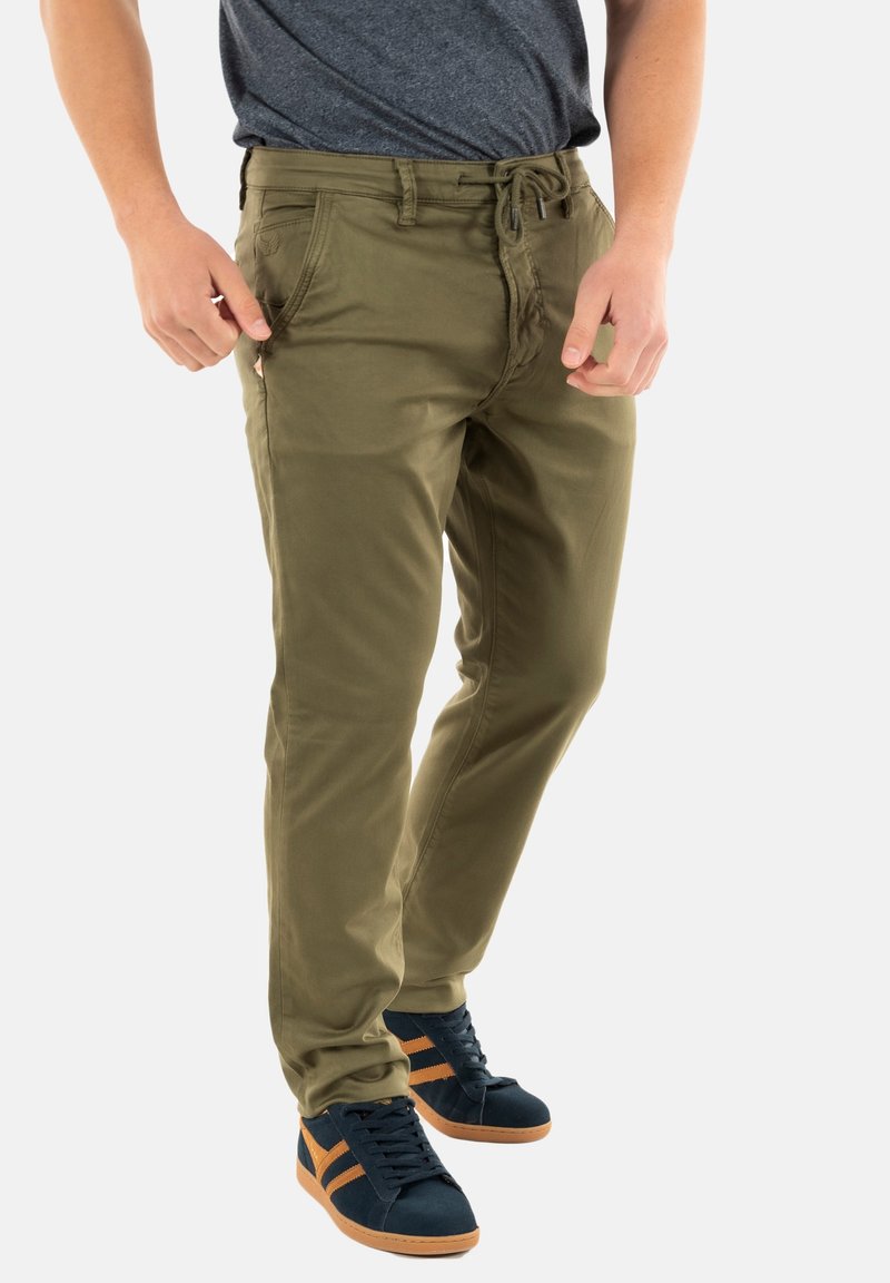 Pantalones verde oliva con un diseño de pierna recta, bolsillos frontales, cordón ajustable, combinados con zapatillas azul marino y naranja.