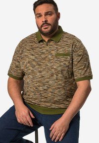 Kortärmad polo med ett flerfärgat texturmönster i jordnära färger, med en grön krage och fickdetalj, kombinerad med mörka jeans.