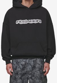 Sweat-shirt à capuche noir avec une poche frontale et un logo "PEGADOR" brodé. Caractérisé par une coupe ample et des poignets côtelés; porté avec un pantalon gris à motif.