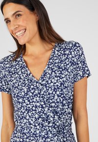 Abito a rapimento floreale blu navy con maniche corte, caratterizzato da piccoli fiori bianchi, una scollatura a V e una cintura in vita per una vestibilità regolabile.