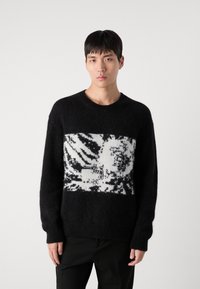 Black knit sweater with a white abstract pattern across the chest, soft texture, crew neck, and ribbed cuffs and hem.