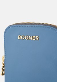 Blue fabric pouch with gold "BOGNER" logo, smooth texture, and contrasting dark zipper. Features a decorative chain element.
