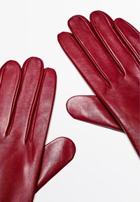 Guanti in pelle rossa con una texture liscia, dita allungate e cuciture visibili sul retro, caratterizzati da un design elegante e aderente.