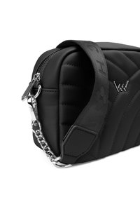 Černá prošívaná taška s hladkým koženým povrchem, stříbrnou kovovou hardware a vzorovaným popruhem s logem značky. Viditelné detaily zipového uzávěru.