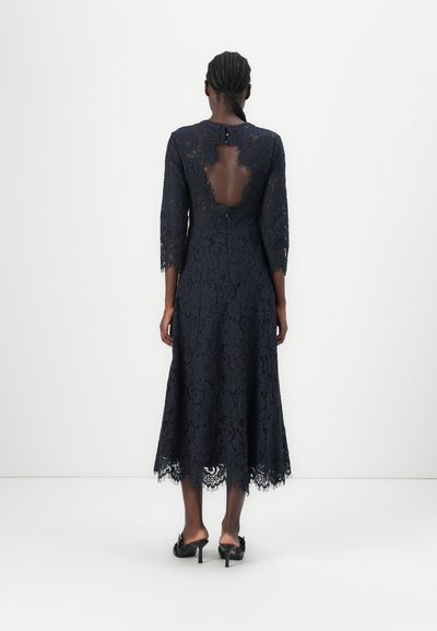 Navy lace dress with a scalloped hem, three-quarter sleeves, and a keyhole back. Intricate floral pattern throughout.