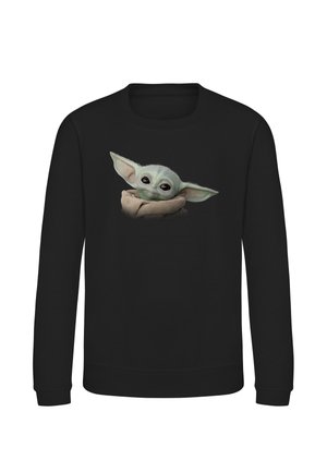 Sort langærmet sweater med en grafik af en lille grøn skabning med store øre indhyllet i et brunt klæde centreret foran.