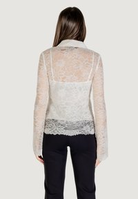Blusa bianca in pizzo con maniche lunghe, motivo floreale e orlo scallopato, dotata di colletto e dettagli posteriori semi-trasparenti.