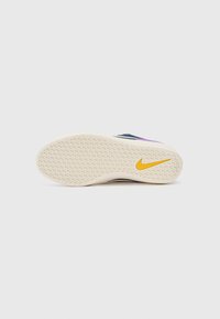 Semelle de basket Nike en blanc cassé avec un motif texturé et un logo swoosh jaune. Présente un accent violet sur le côté.