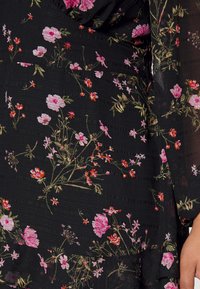 Robe noire à imprimé floral avec des fleurs roses et rouges. Tissu texturé avec un ourlet volé et des manches longues transparentes.