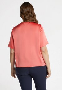 Top corto in satin corallo con maniche corte, scollatura rotonda, texture liscia e vestibilità comoda, abbinato a pantaloni navy. Nessun motivo o accessorio visibile.