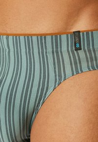 Männerbriefs in hellblau mit vertikalen schwarzen Streifen. Sie verfügen über eine glatte Textur und einen kontrastierenden orangen Bund mit einem Etikett.