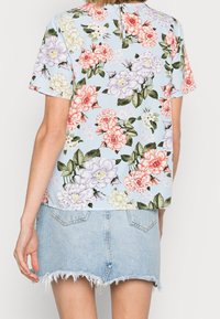 Femme portant un haut à manches courtes floral bleu pastel et une mini-jupe en jean déchirée bleu clair, vue de dos.