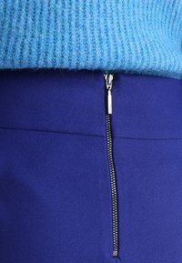 Pull en laine bleu associé à une jupe crayon lisse et bleu profond avec un détail de fermeture éclair argentée sur le côté. Contrastes de textures entre les matériaux.