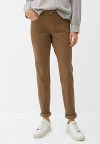 Brązowe spodnie o zwężanym kroju wykonane z mieszanki bawełny, z frontowymi kieszeniami, podwiniętymi mankietami i metalowym zapięciem, połączone z białymi sneakersami.