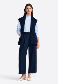 Chaleco navy con hombreras sobre una camisa de rayas azul claro, combinado con pantalones de pierna ancha de talle alto navy y mules de tacón bloque en color crema.