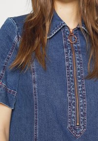 Jeansskjorta med korta ärmar, med en dragkedja framtill med ett rundat handtag, kontrasterande röda stygn och en klassisk kragdesign.