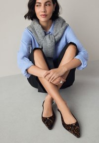 Scarpe slingback con punta a punta nere e marroni con motivo leopardato, caratterizzate da un accento metallico e una texture in tessuto morbido.