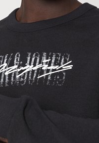 Felpa nera in cotone, con un audace design grafico di testo bianco. Include un colletto e polsini a coste.