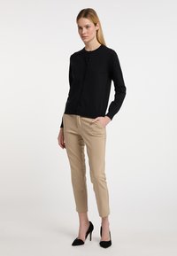 Cardigan negru cu nasturi, guler rotund, asortat cu pantaloni bej, croiți. Modelul poartă pantofi cu toc înalt, vârful ascuțit, negri. Textură netedă.